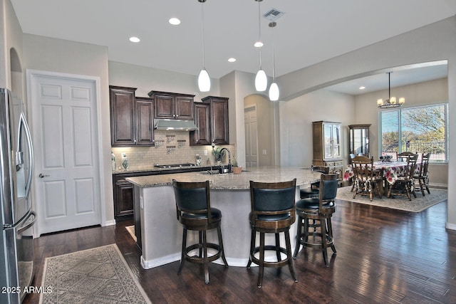 kitchen with a breakfast bar area, a large island with sink, dark hardwood / wood-style flooring, pendant lighting, and stainless steel appliances