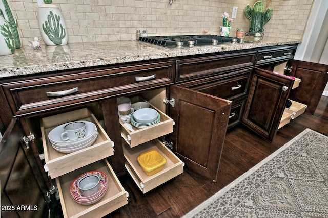 details with dark brown cabinetry, dark hardwood / wood-style flooring, stainless steel gas cooktop, and backsplash