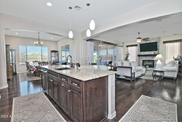 kitchen featuring dark brown cabinetry, sink, decorative light fixtures, a center island with sink, and light stone countertops