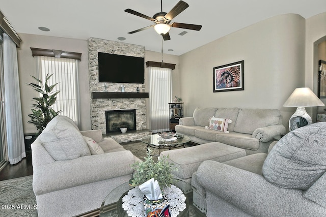 living room featuring hardwood / wood-style flooring, ceiling fan, and a stone fireplace