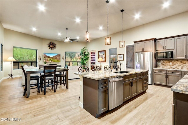 kitchen with an island with sink, appliances with stainless steel finishes, backsplash, hanging light fixtures, and sink