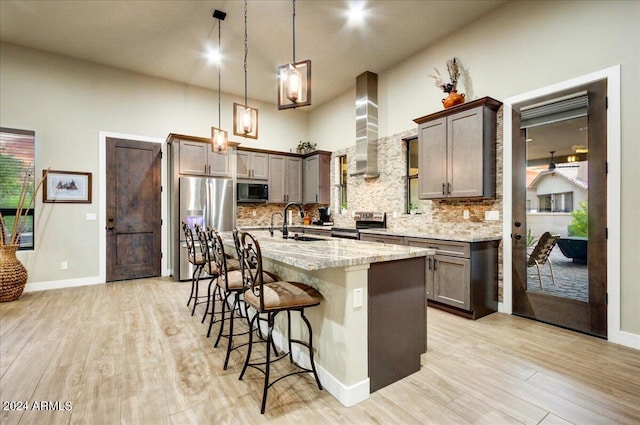 kitchen with a high ceiling, a kitchen bar, stainless steel appliances, an island with sink, and hanging light fixtures