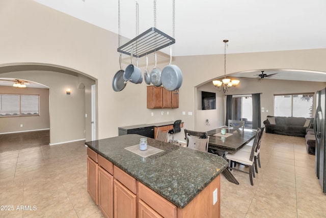 kitchen featuring arched walkways, dark stone counters, lofted ceiling, a kitchen island, and open floor plan