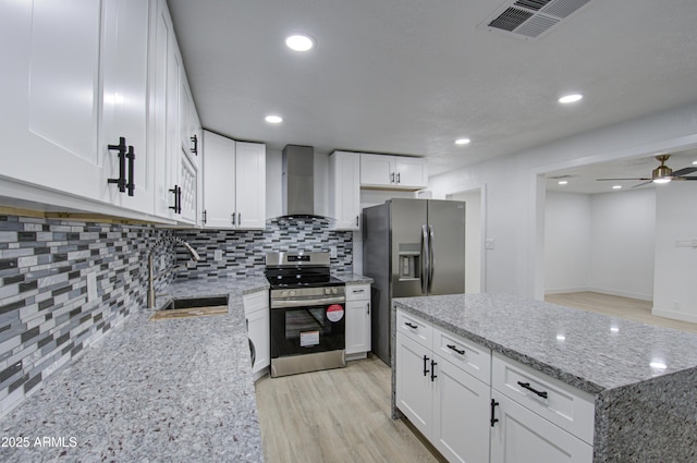 kitchen with appliances with stainless steel finishes, white cabinetry, sink, light stone counters, and wall chimney exhaust hood