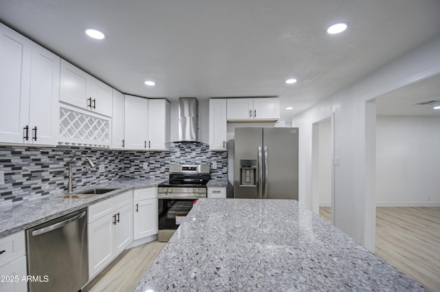 kitchen featuring white cabinetry, appliances with stainless steel finishes, light stone counters, and wall chimney range hood