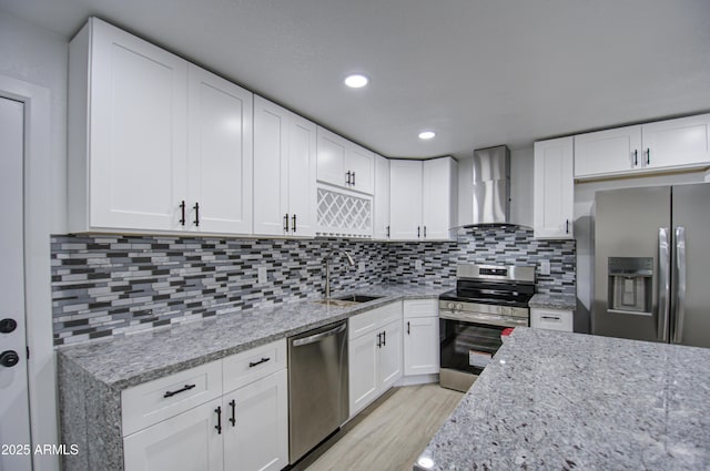 kitchen with appliances with stainless steel finishes, sink, white cabinets, light stone countertops, and wall chimney range hood