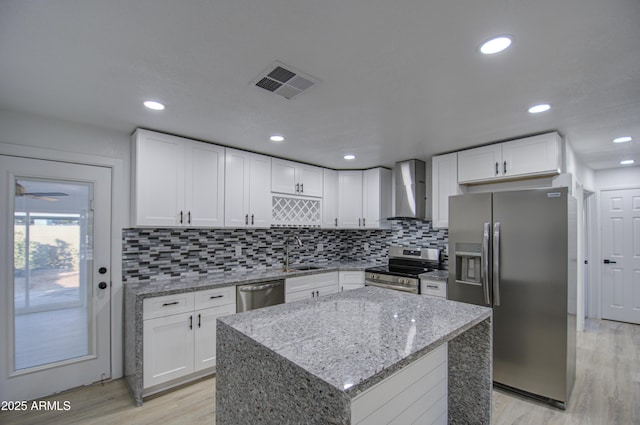 kitchen featuring appliances with stainless steel finishes, light stone countertops, white cabinets, a kitchen island, and wall chimney exhaust hood