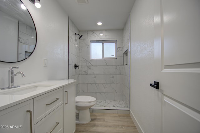 bathroom featuring vanity, hardwood / wood-style floors, toilet, and tiled shower