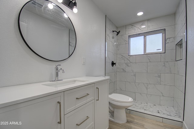 bathroom featuring vanity, wood-type flooring, toilet, and tiled shower