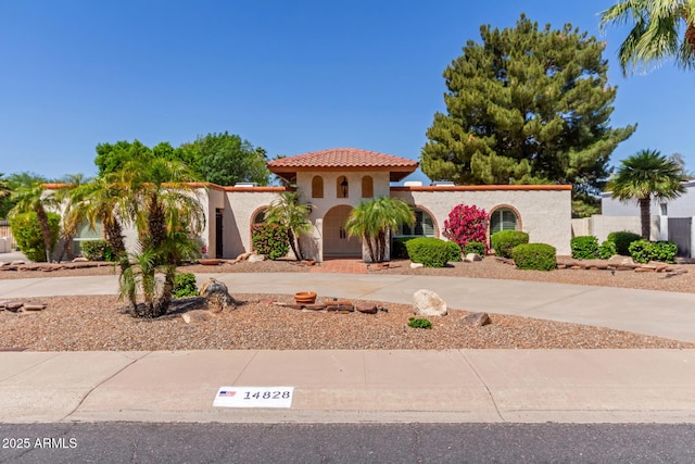 mediterranean / spanish house with curved driveway, stucco siding, a tile roof, and fence