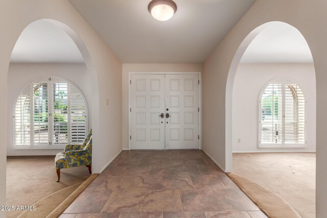 foyer entrance featuring carpet flooring, baseboards, stone finish flooring, and arched walkways