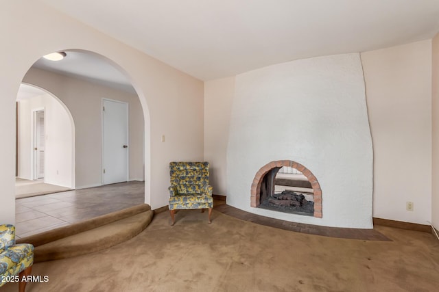 unfurnished room featuring carpet floors, arched walkways, a fireplace with flush hearth, and baseboards