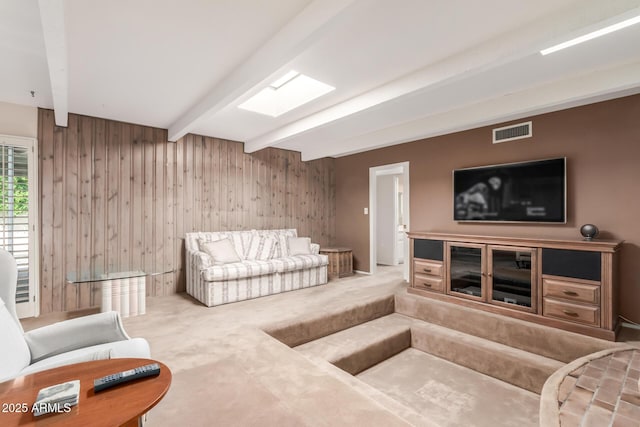 carpeted living room featuring beam ceiling and wood walls