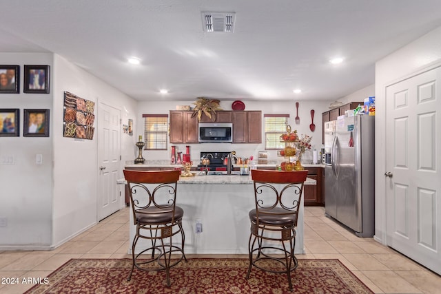 kitchen with appliances with stainless steel finishes, a center island with sink, a kitchen breakfast bar, and light tile patterned flooring