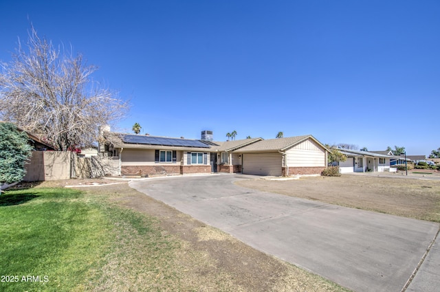 single story home with an attached garage, brick siding, driveway, roof mounted solar panels, and a front yard