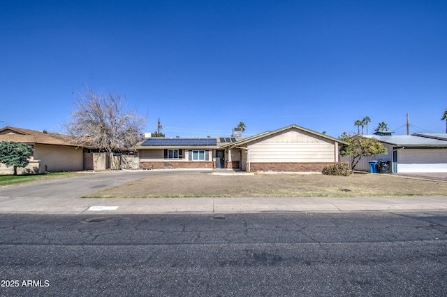 single story home with aphalt driveway, roof mounted solar panels, brick siding, and fence