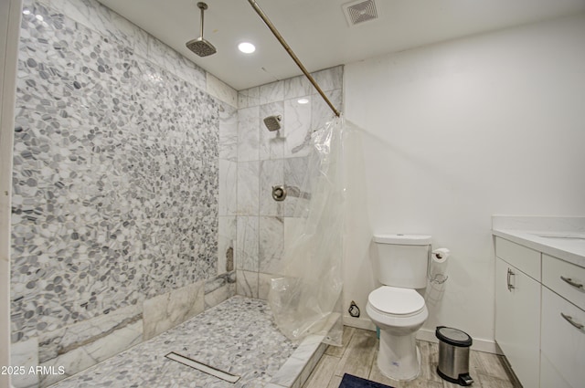 bathroom featuring visible vents, toilet, a tile shower, vanity, and wood finish floors