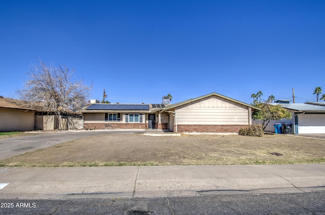 single story home featuring roof mounted solar panels, brick siding, fence, and concrete driveway