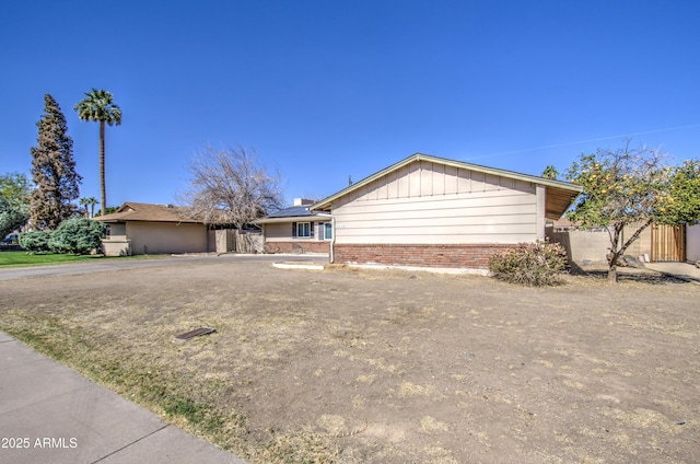 ranch-style house with driveway, brick siding, board and batten siding, and fence