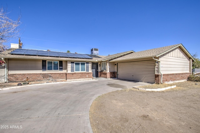 ranch-style home featuring an attached garage, solar panels, brick siding, concrete driveway, and board and batten siding