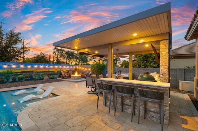 patio terrace at dusk with exterior bar and a fire pit