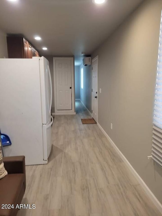 interior space with white fridge, a wall unit AC, and light hardwood / wood-style flooring