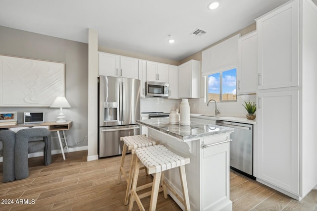 kitchen with a breakfast bar area, stainless steel appliances, a sink, a kitchen island, and white cabinets