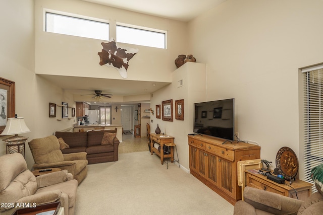 living area featuring a ceiling fan, visible vents, light colored carpet, and a towering ceiling