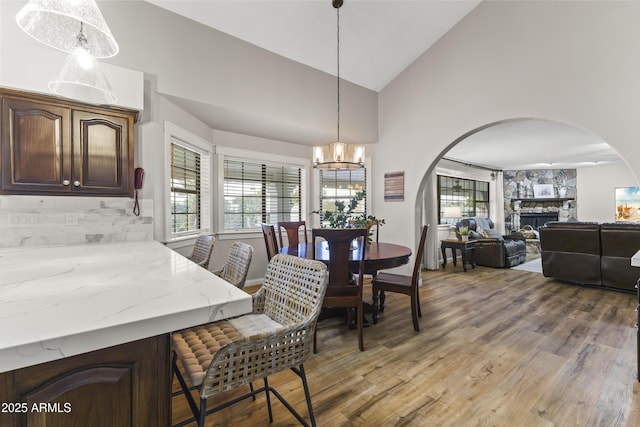 dining room with lofted ceiling, a fireplace, a notable chandelier, and light hardwood / wood-style flooring