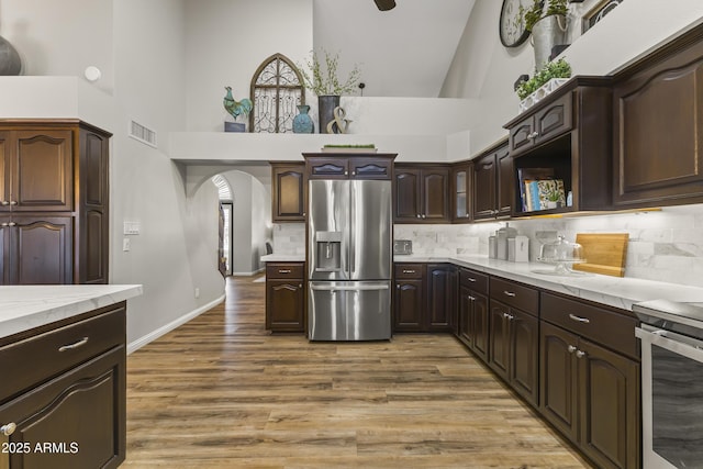 kitchen with a towering ceiling, wood-type flooring, stainless steel fridge, decorative backsplash, and dark brown cabinetry