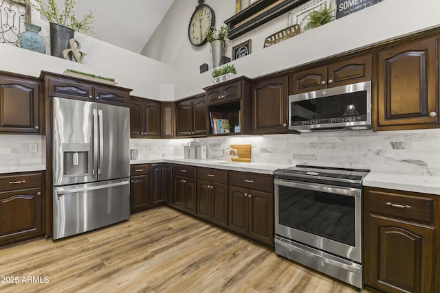 kitchen with high vaulted ceiling, backsplash, stainless steel appliances, dark brown cabinets, and light wood-type flooring