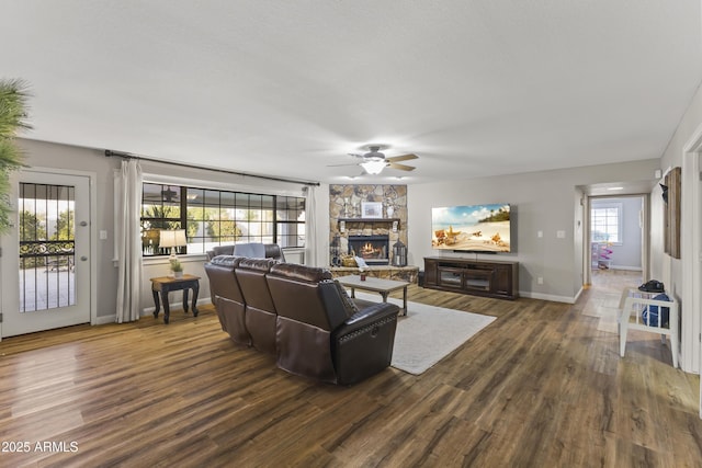 living room with a healthy amount of sunlight, a stone fireplace, and dark hardwood / wood-style floors