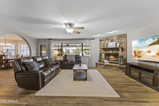 living room featuring a stone fireplace, dark wood-type flooring, and ceiling fan with notable chandelier