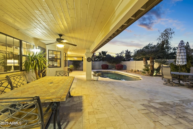 patio terrace at dusk featuring a fenced in pool and ceiling fan