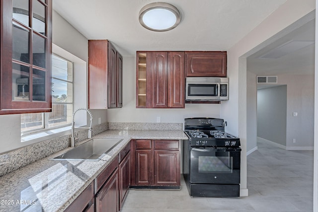 kitchen featuring light stone countertops, black gas stove, and sink