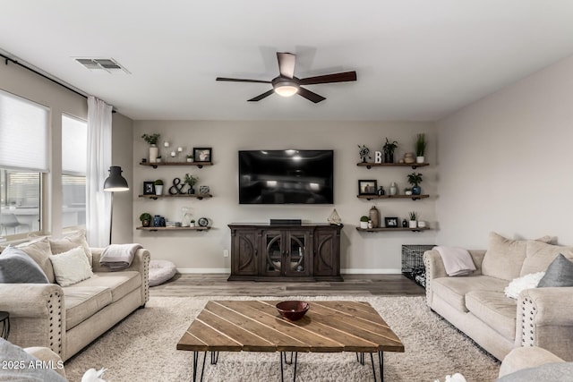 living room with a ceiling fan, visible vents, baseboards, and wood finished floors