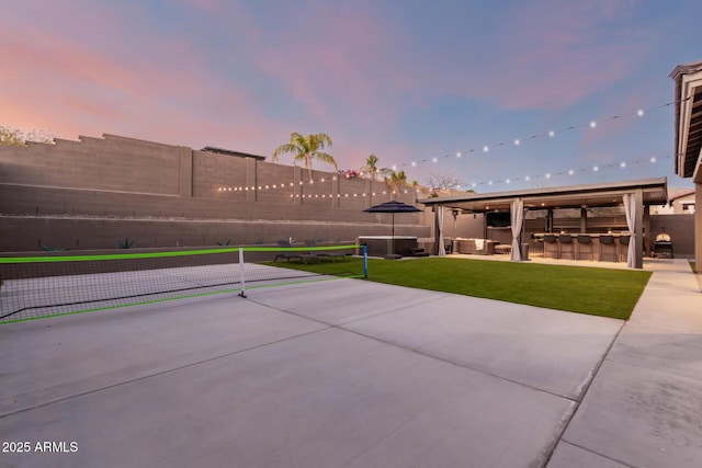 patio terrace at dusk featuring a fenced backyard, outdoor dry bar, a lawn, and an outdoor living space