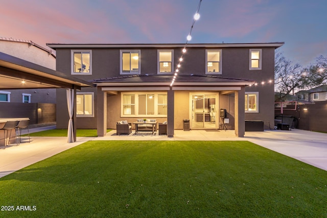 back of property at dusk with a lawn, fence, a patio area, outdoor lounge area, and stucco siding