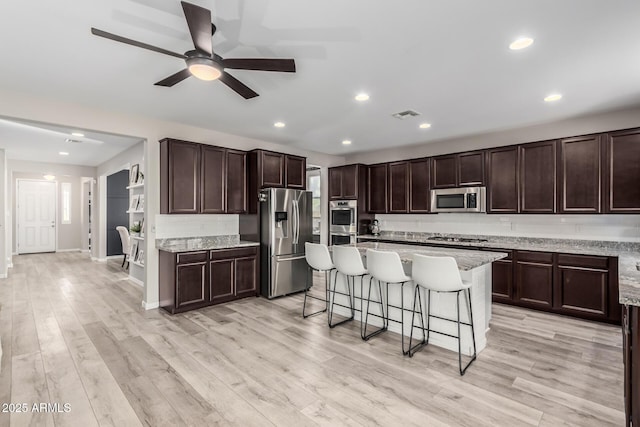 kitchen with stainless steel appliances, tasteful backsplash, dark brown cabinets, and a kitchen breakfast bar