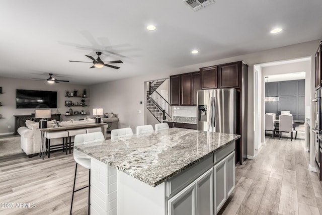 kitchen with a breakfast bar area, light stone countertops, visible vents, and stainless steel fridge with ice dispenser