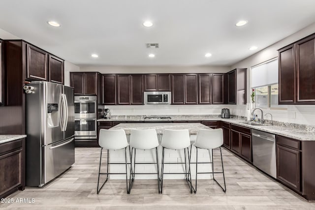 kitchen featuring dark brown cabinetry, visible vents, a breakfast bar area, stainless steel appliances, and a sink