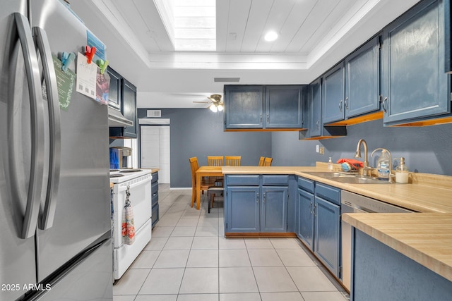 kitchen featuring light tile patterned flooring, blue cabinets, sink, appliances with stainless steel finishes, and a tray ceiling