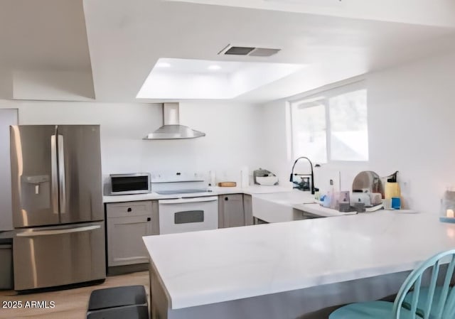 kitchen with stainless steel fridge, wall chimney exhaust hood, electric range, a sink, and a peninsula