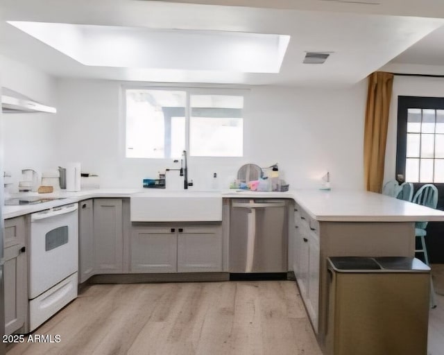 kitchen featuring a peninsula, stainless steel dishwasher, light wood-style floors, a sink, and under cabinet range hood