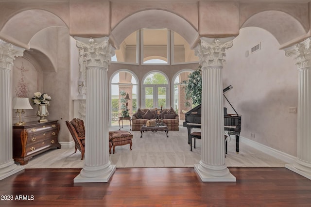 living area featuring decorative columns, a high ceiling, visible vents, and wood finished floors