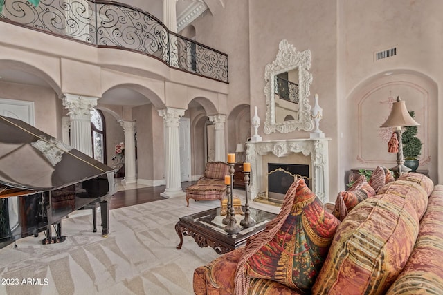 interior space featuring visible vents, a premium fireplace, wood finished floors, a high ceiling, and ornate columns