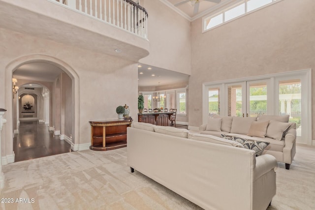 living area featuring arched walkways, ceiling fan with notable chandelier, a high ceiling, carpet flooring, and baseboards