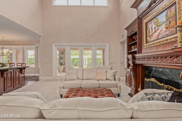 living room featuring a chandelier, a towering ceiling, a high end fireplace, baseboards, and french doors