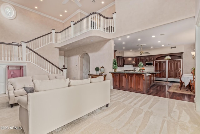 living area with ceiling fan, a high ceiling, crown molding, and carpet flooring