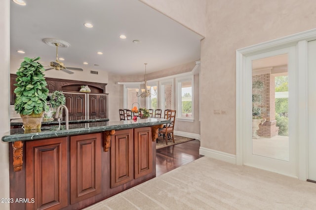 kitchen with pendant lighting, brown cabinets, recessed lighting, dark carpet, and dark stone countertops